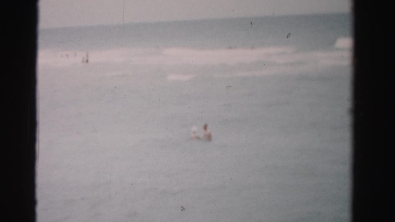 Ocean water and pale surf with small distant figures near the horizon.