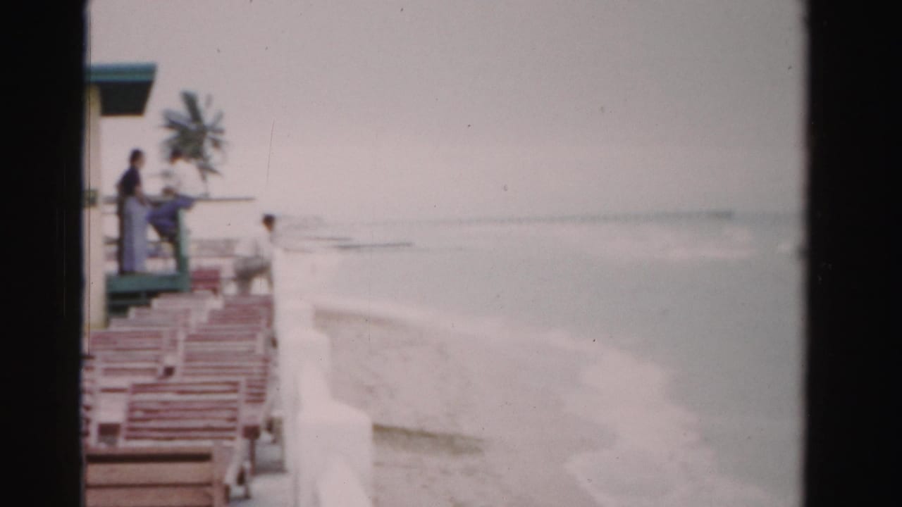 Beach chairs beside a lifeguard station with ocean surf and a few people nearby.
