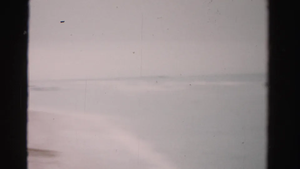 Soft 8mm view of the Dade County beach shoreline in 1955, with surf, sand, and beach seating along the edge of frame.