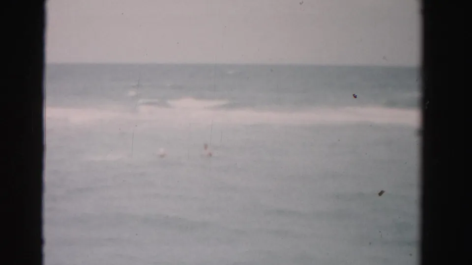 1955 Dade County, Florida ocean view with breaking waves and two small swimmers in the water, filmed in soft 8mm color.