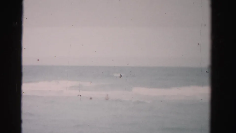 1955 Dade County ocean frame with distant swimmers, gentle breaking waves, and visible 8mm dust marks.