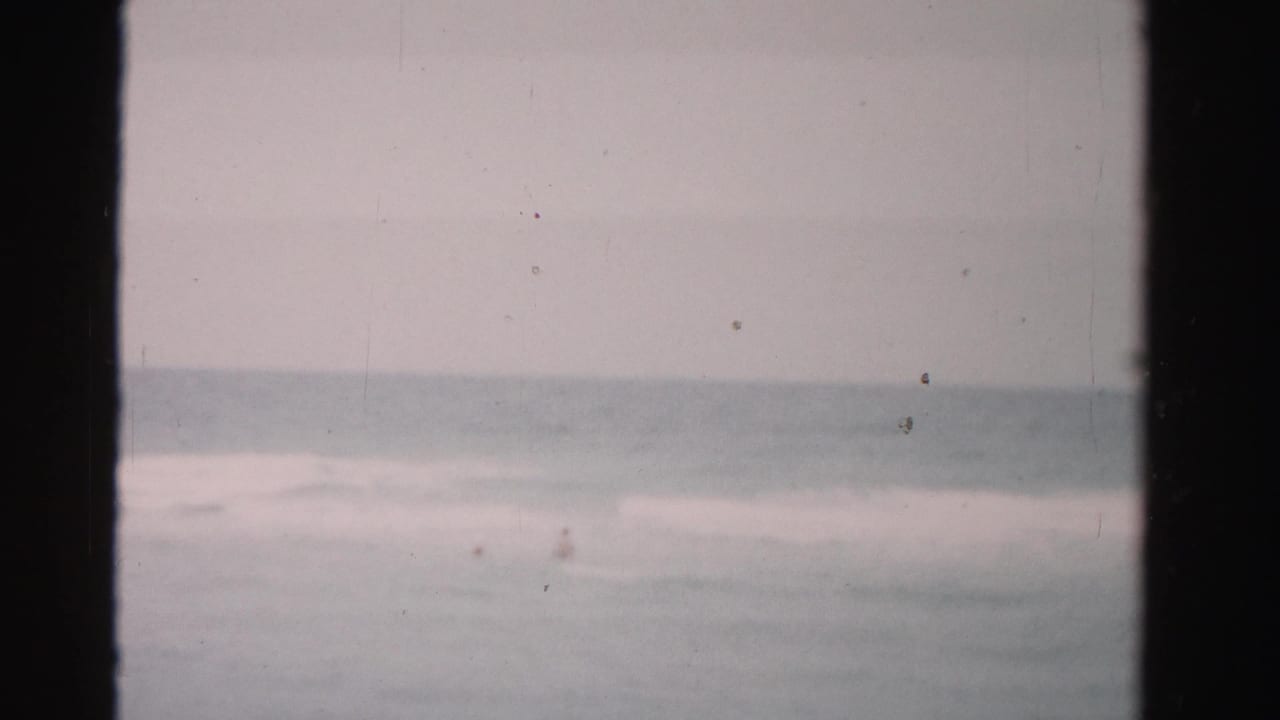 Ocean horizon and surf seen through dark 8mm film frame edges.