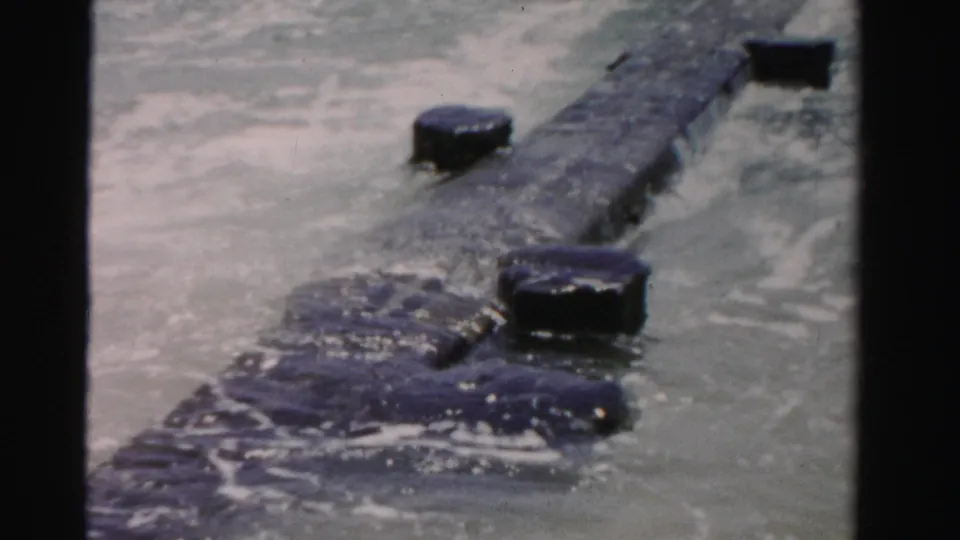 1955 Dade County 8mm frame showing a long dark object partly submerged as ocean waves move around it.