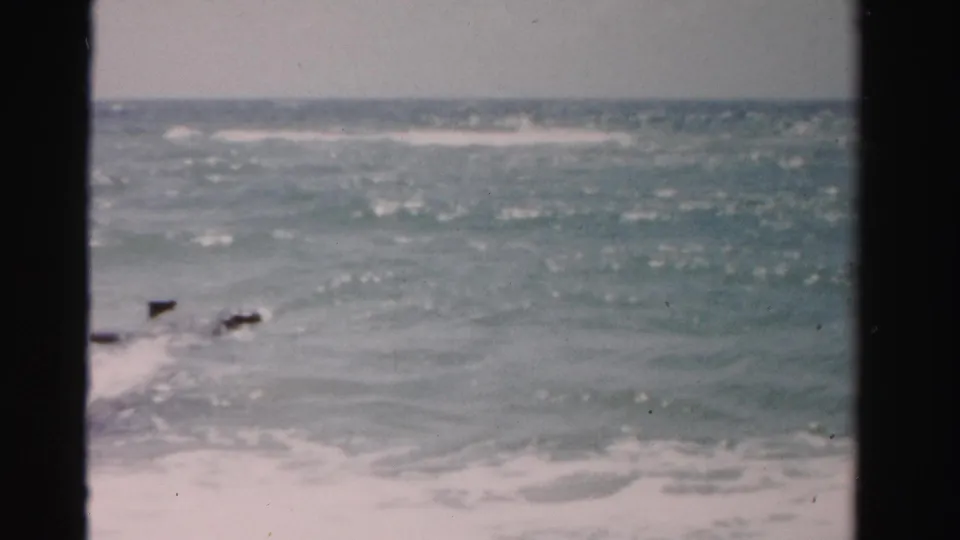 A wider 1955 Dade County ocean view shows the horizon, rolling surf, and small dark fragments near the lower edge.