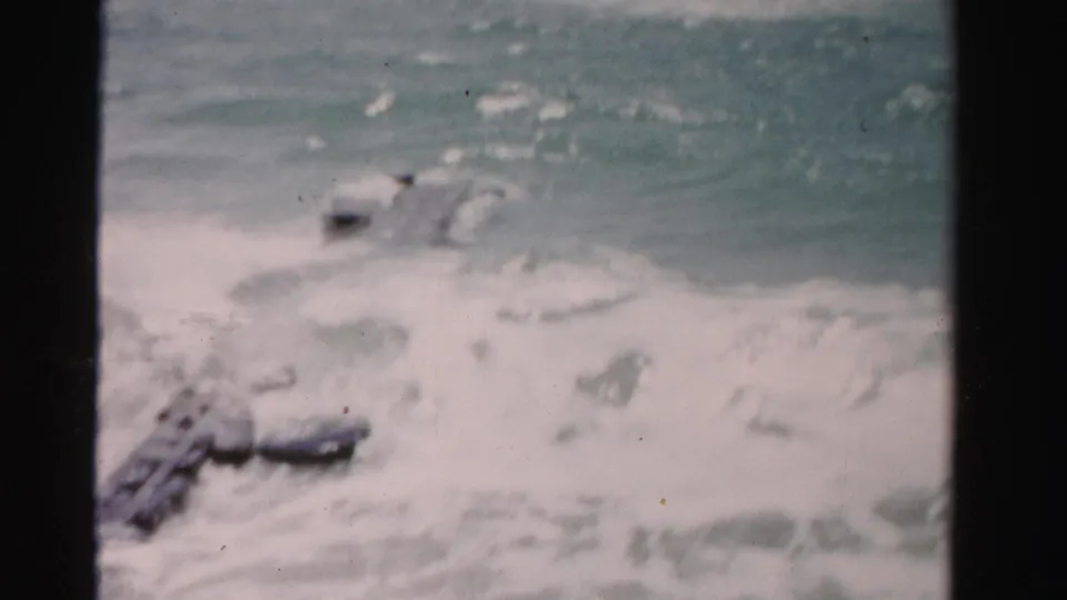1955 Dade County, Florida home-movie frame of rough ocean water breaking over a rocky jetty with heavy white foam in front.