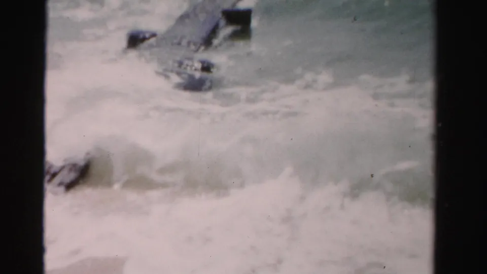 1955 Dade County, Florida 8mm frame showing foamy ocean water washing around dark wooden deck posts or planks.