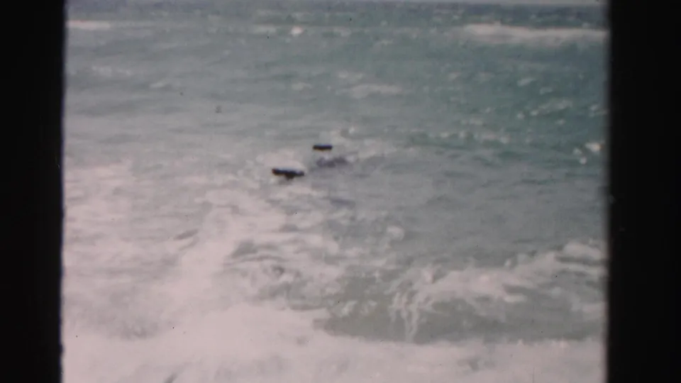 1955 Dade County, Florida 8mm frame showing choppy sea, white foam, and small dark deck elements amid the waves.