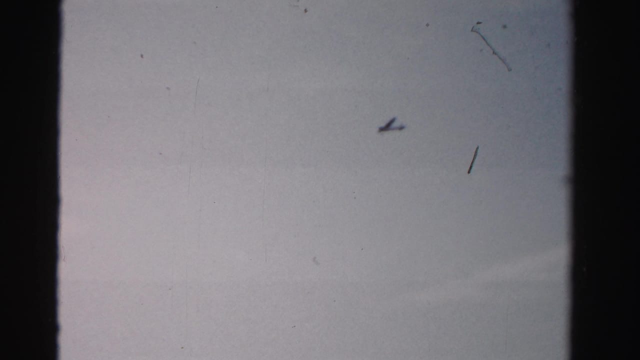 Small airplane silhouette crossing a pale sky with film edge visible.