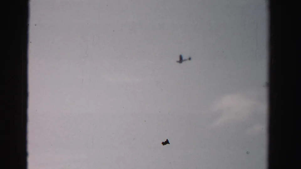 Small single-engine airplane appears high in the frame against open sky in archival 8mm footage from Dade County, Florida.