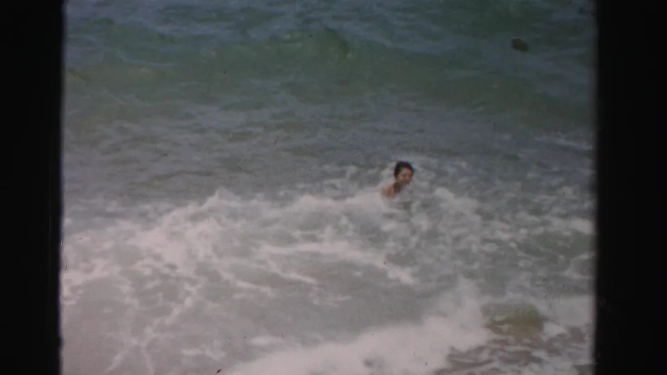 A swimmer appears partly submerged in the Dade County ocean surf, with waves and foam filling the frame.