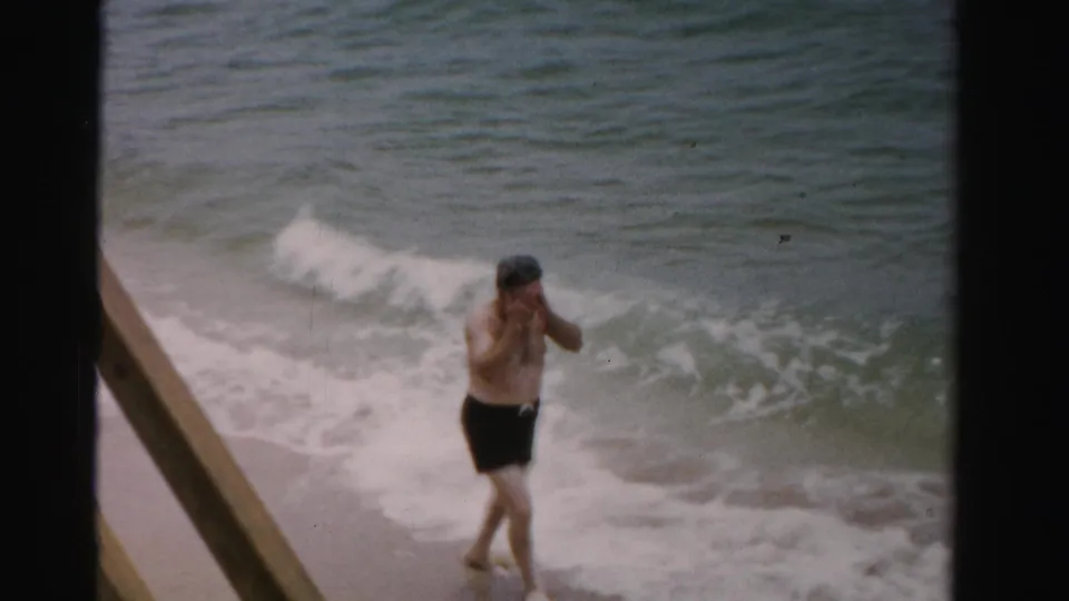 A man in dark swim trunks walks along the wet shoreline as waves roll behind him in Dade County, Florida.