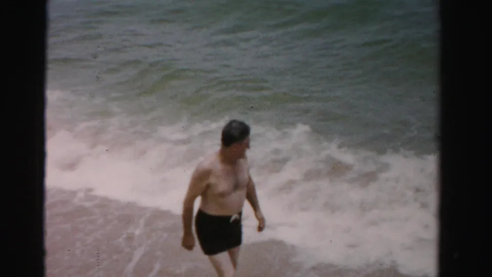 Man in swim trunks walks through shallow surf on a Florida beach in 1955 home-movie footage.