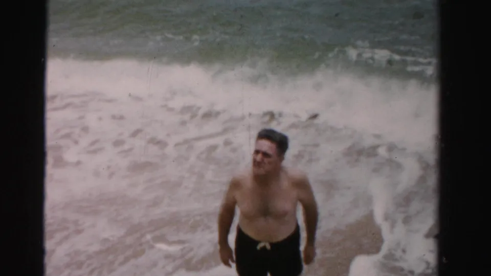 Closer 8mm frame of a man at the surf edge with foamy water filling the background.