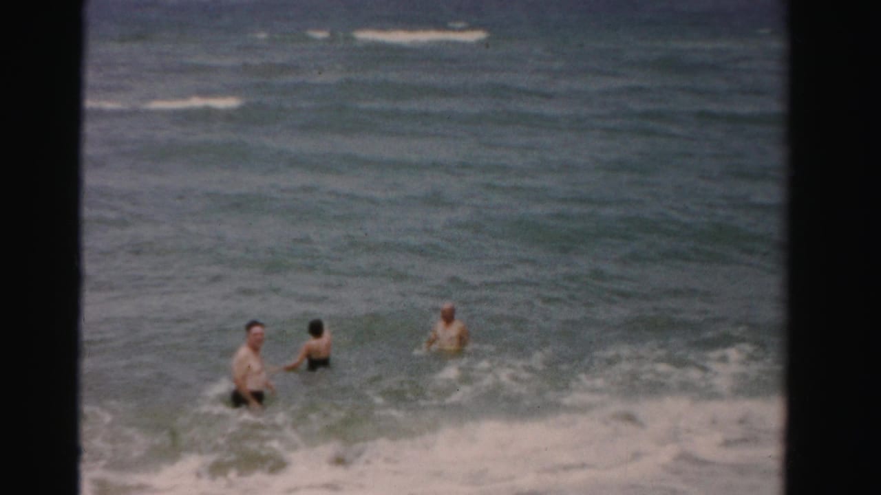 Three adults stand in waist-deep surf as waves move behind them.
