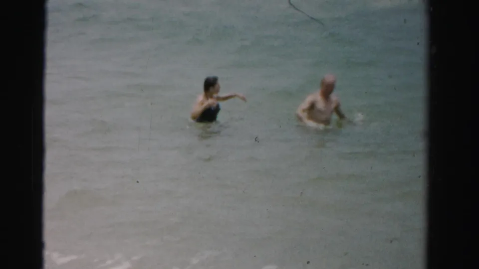 The woman appears to gesture toward the water while the man stands nearby in this 1955 Dade County beach home movie frame.