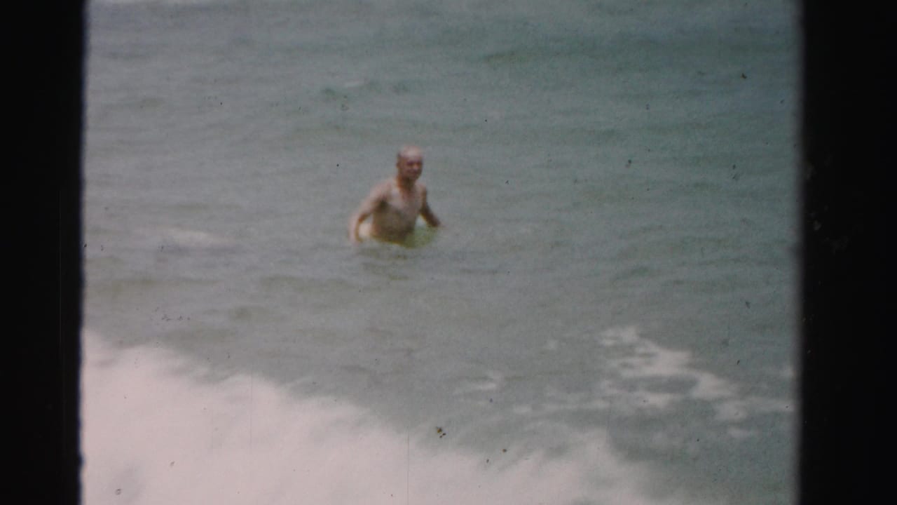 1955 Dade County 8mm frame showing a shirtless man wading alone in muted blue-green ocean water.