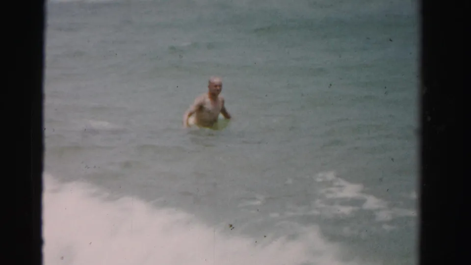 1955 Dade County 8mm frame showing a shirtless man wading alone in muted blue-green ocean water.