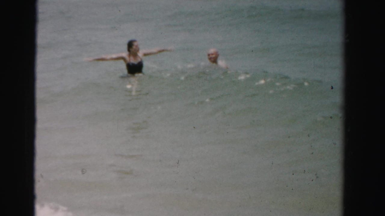 Woman in a dark swimsuit and shirtless man swimming in open ocean water.