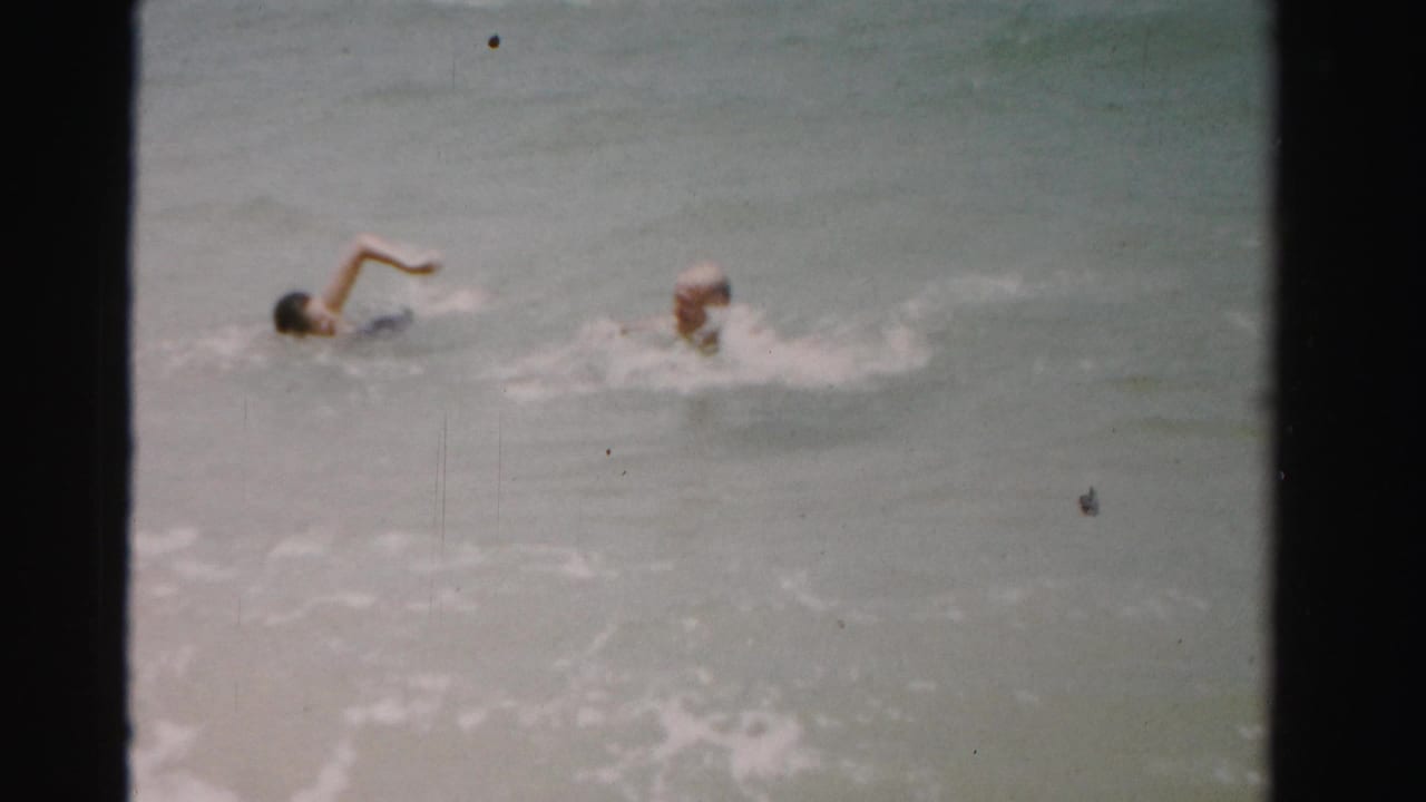 Two swimmers in the surf, one with an arm raised during a stroke.