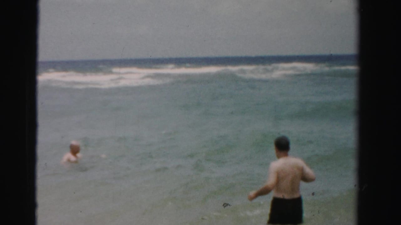 Two adults are in the ocean, one closer to camera and one farther out in the water.