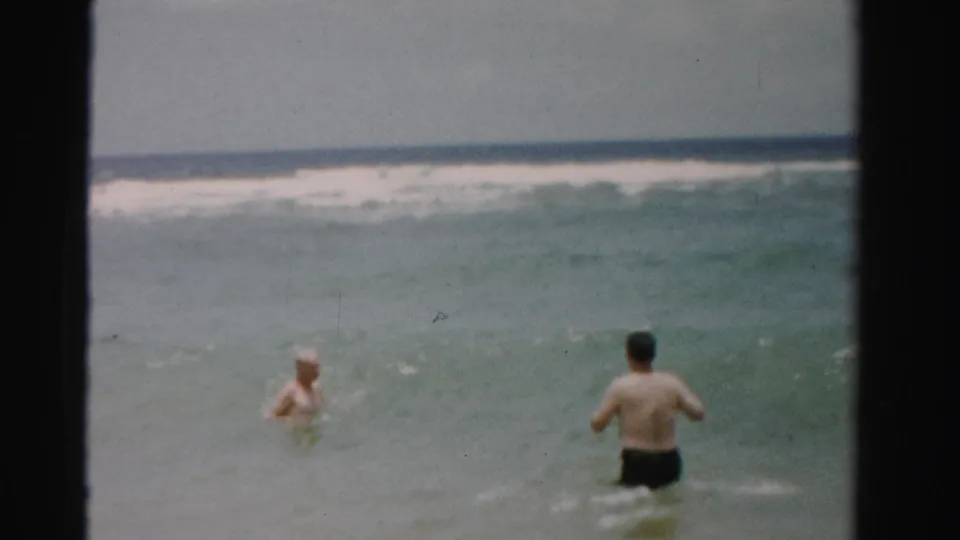 1955 Dade County surf scene with two adults wading apart in shallow water, framed by a flat horizon and pale sky.