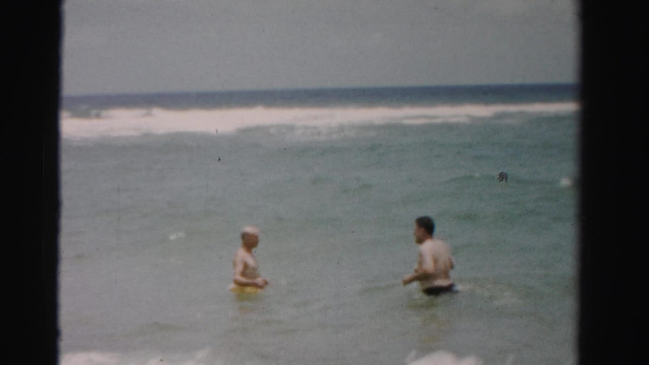 Two men face each other in waist-deep ocean water near rolling surf.