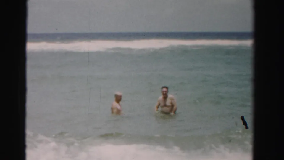 The clip ends with two adult men in waist-deep ocean water, one turning toward camera, in 1955 Dade County home-movie footage.
