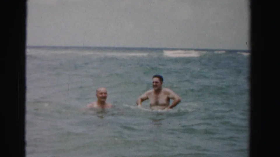 Two adult men swim or stand in the ocean off Dade County, Florida, in 1955 home-movie footage.
