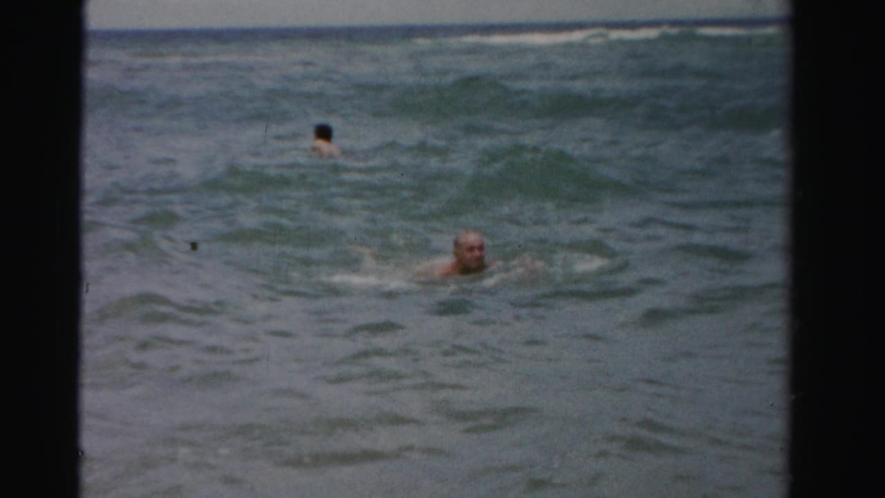 Older man swims in choppy ocean water while another swimmer is farther offshore.