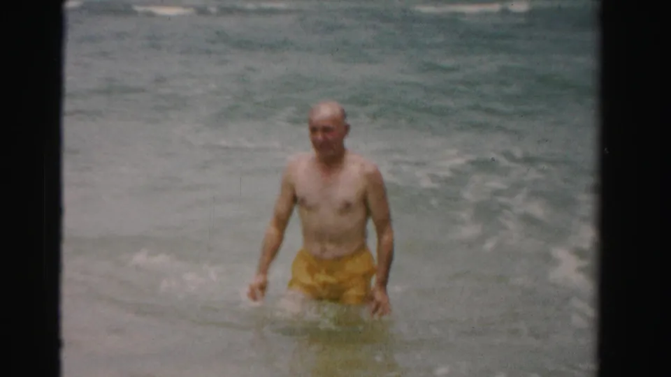 Older man in yellow swim trunks wades through shallow ocean water in 1955 Dade County, Florida home-movie footage.