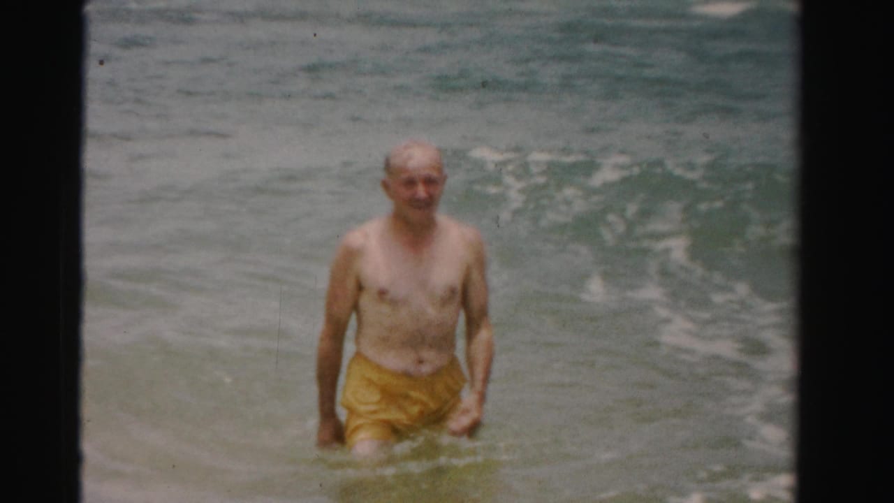 Older man smiling while standing in ocean water near small waves.