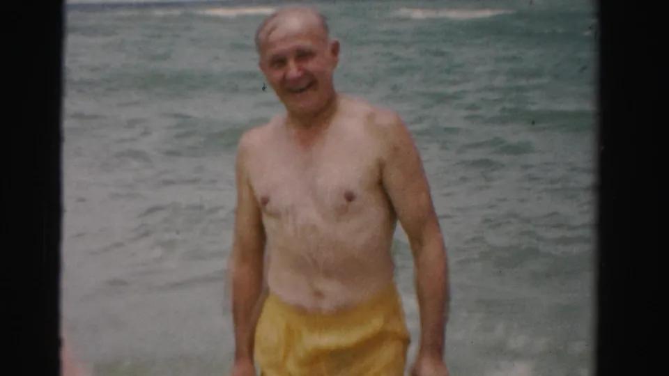 Older man approaches the camera through shallow ocean surf in 1955 Dade County, Florida home-movie footage.