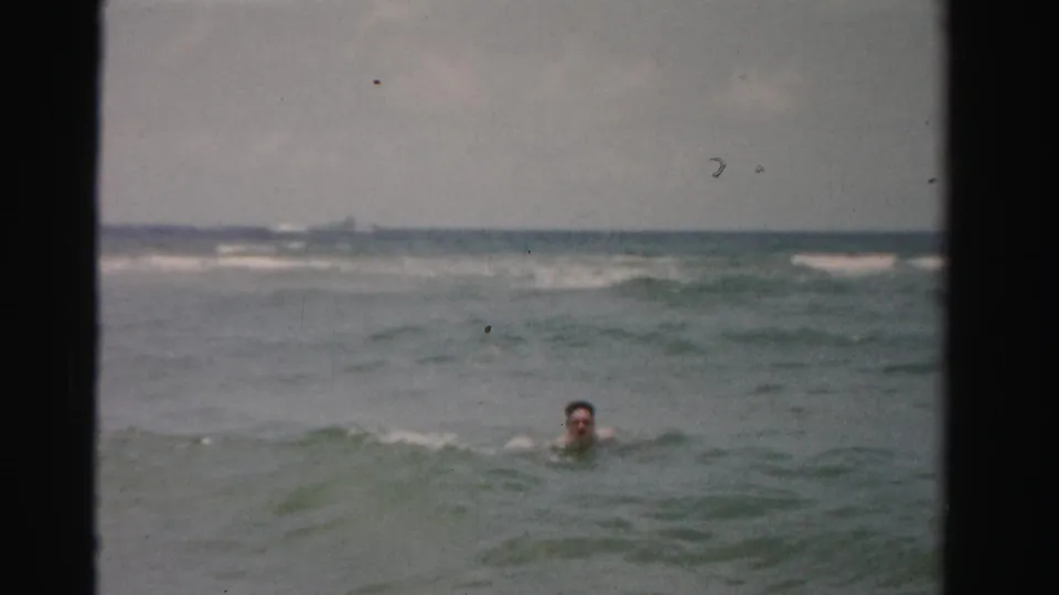 A swimmer appears farther from the camera, with only head and shoulders visible among gray-green ocean waves.