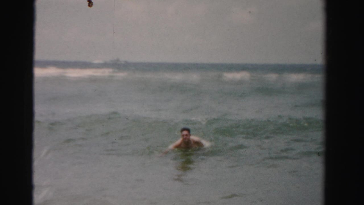 Adult man swimming in choppy ocean water under a hazy horizon.