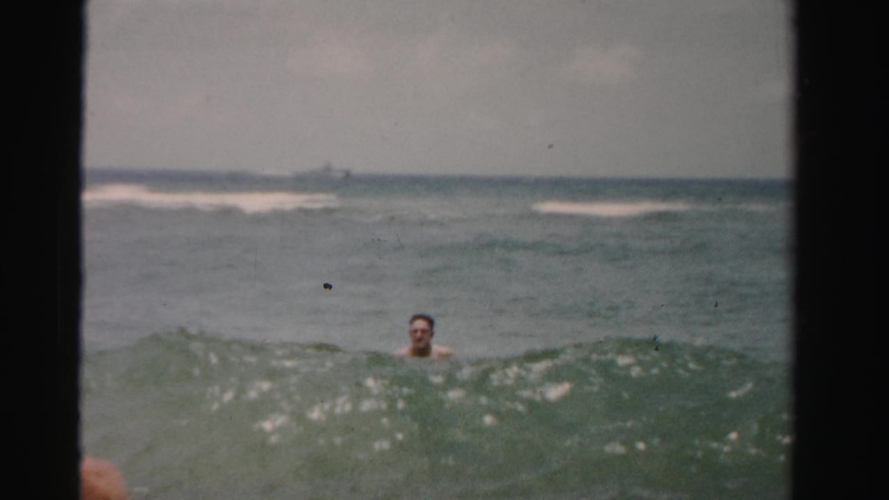 Adult man partly submerged in a wave with open ocean behind him.