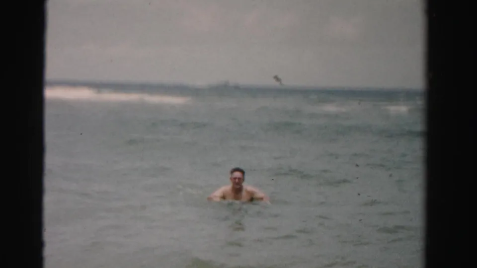 Adult swimmer faces the camera in Dade County ocean water, with low surf and a pale horizon in the background.
