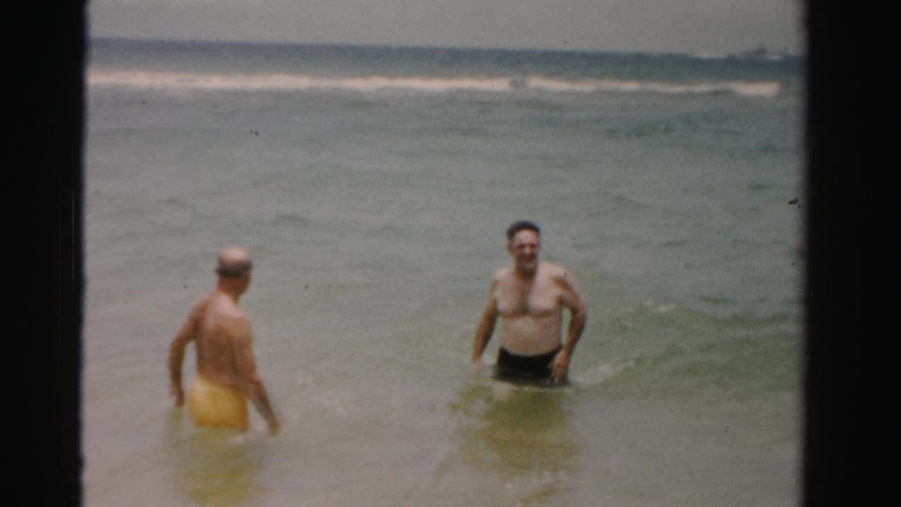 1955 Dade County, Florida beach footage with two adult men in swim trunks standing in shallow water near rolling surf.