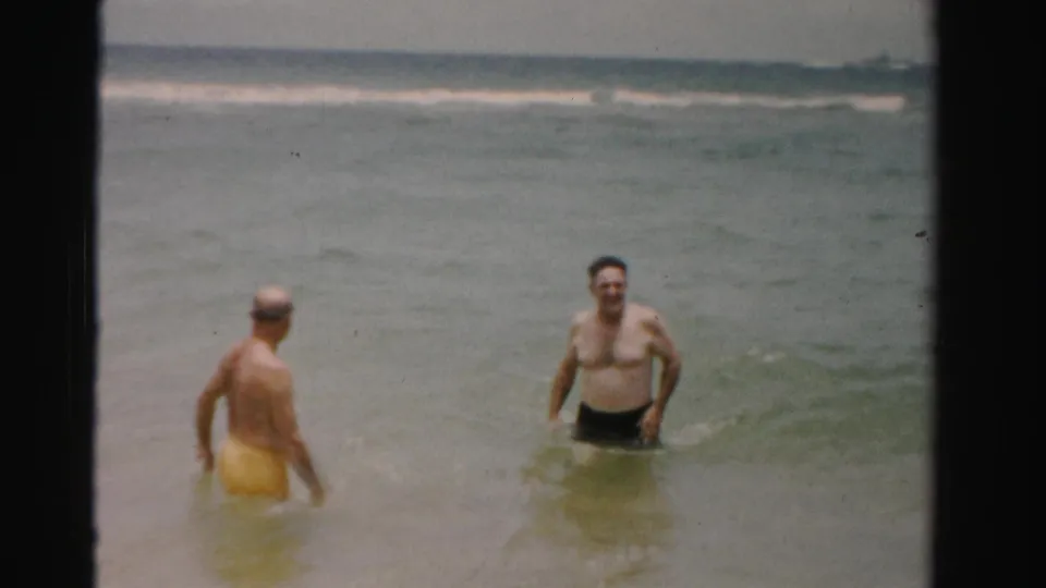 1955 Dade County, Florida beach footage with two adult men in swim trunks standing in shallow water near rolling surf.