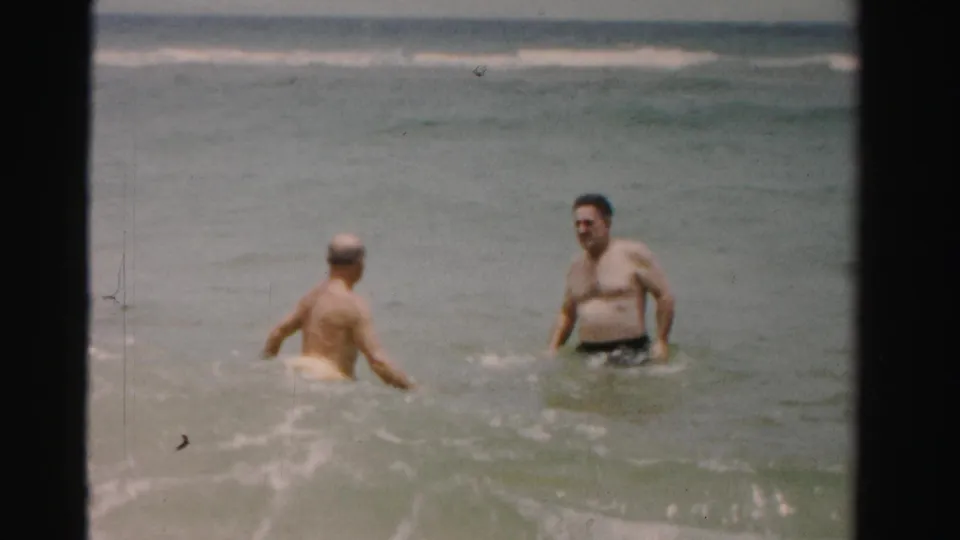 1955 Dade County, Florida 8mm still showing two adult men separated in waist-deep ocean water with surf rolling behind them.