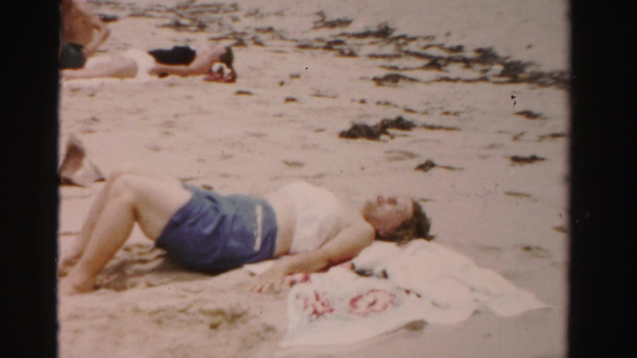Woman sunbathes on sand near towels and seaweed.