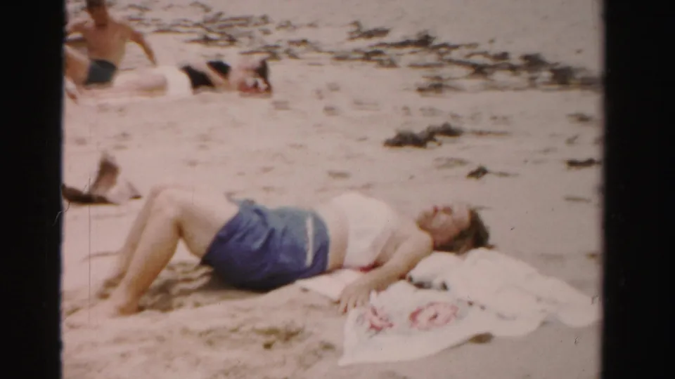 A sunbathing woman lies on a towel-strewn sandy beach in Dade County, Florida, with other bathers partly visible behind her.