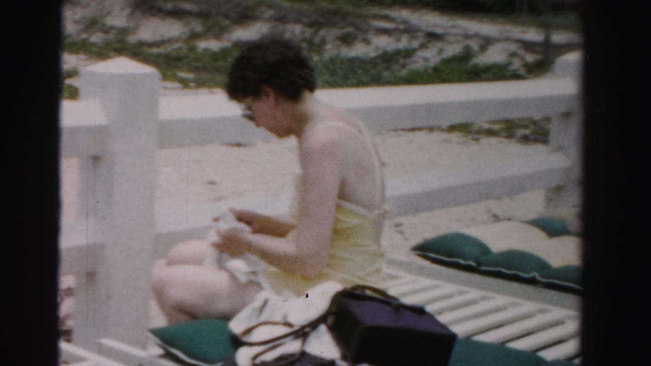 Woman in a yellow swimsuit sits on a white lounge chair and handles a towel.