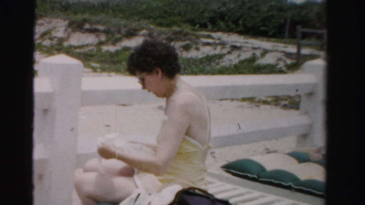 Woman in a yellow swimsuit sits on a lounge chair near a beach wall.