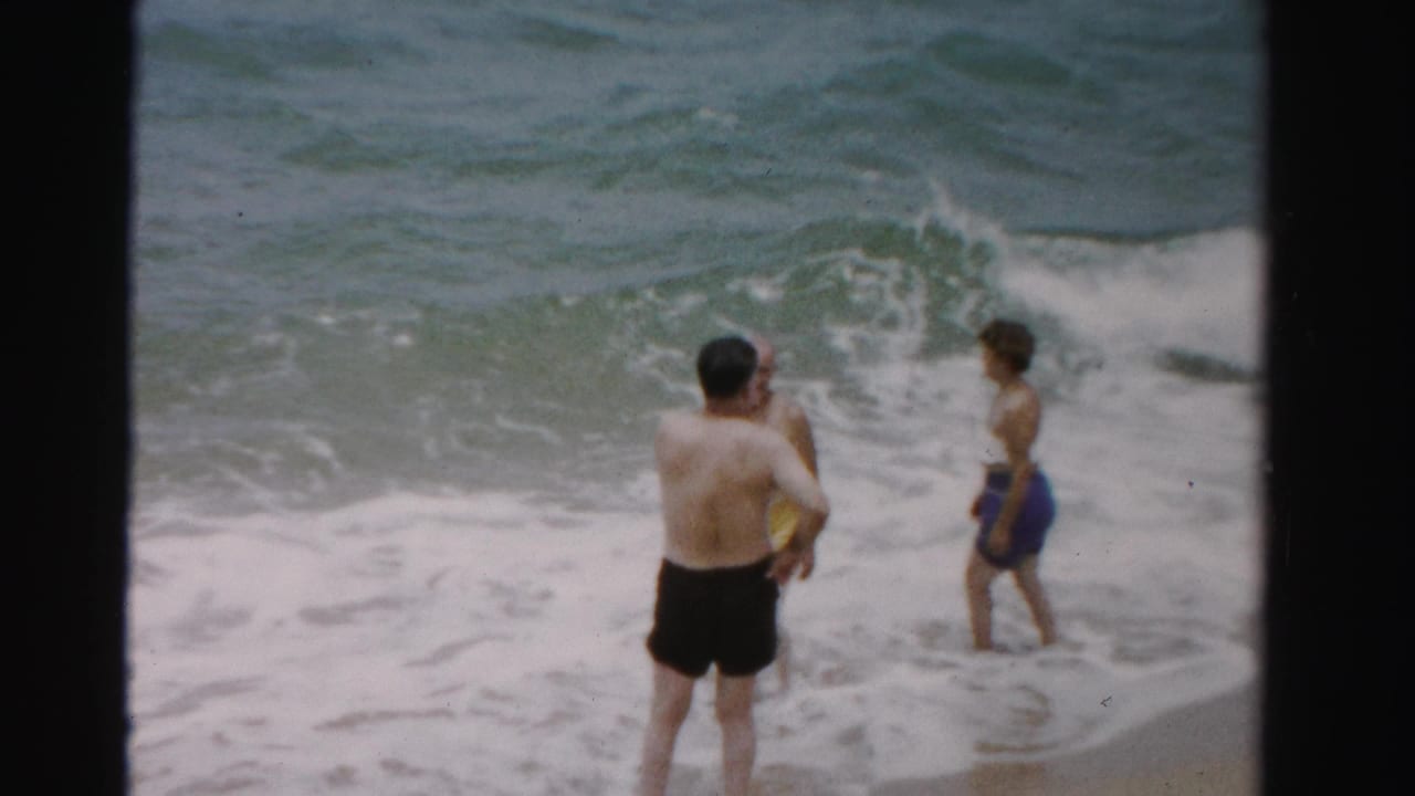Three adults stand and wade at the edge of ocean surf.