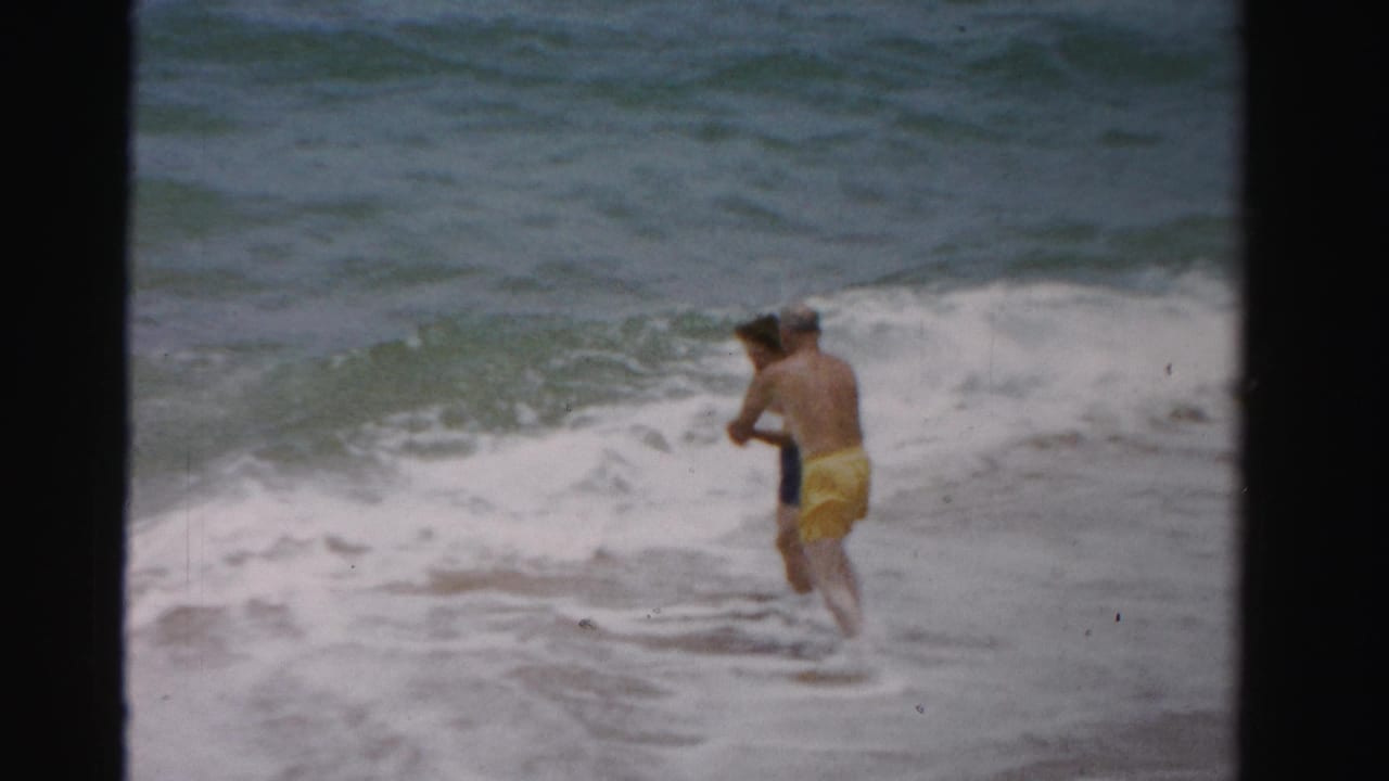 A man and woman move together through breaking surf near shore.