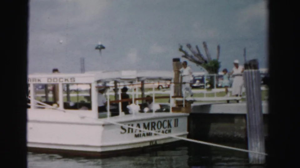 A small passenger boat marked Shamrock II sits at a Dade County dock while people stand and sit around the pier area.