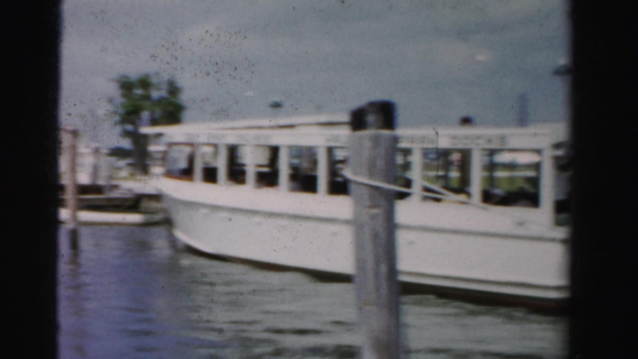 White ferry at the dock seen behind a large piling with calm water in front.