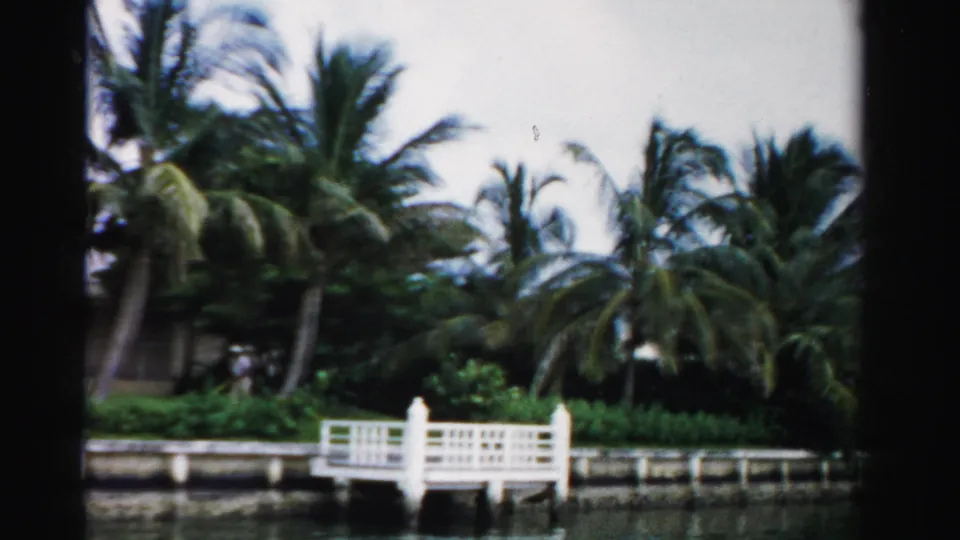 1955 Florida home-movie frame with a white dock, palms, seawall, and canal water in a residential setting.