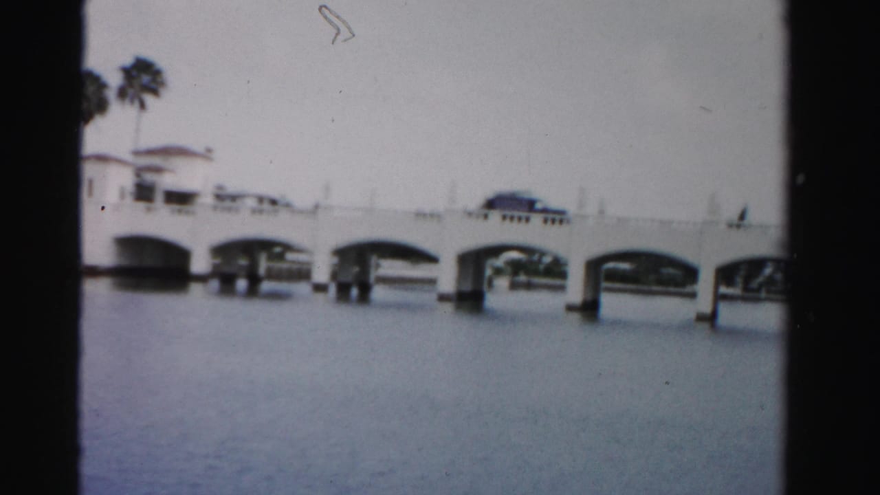 1955 Dade County view of a white multi-arch bridge over still water, with palms and a dark car visible on the span.
