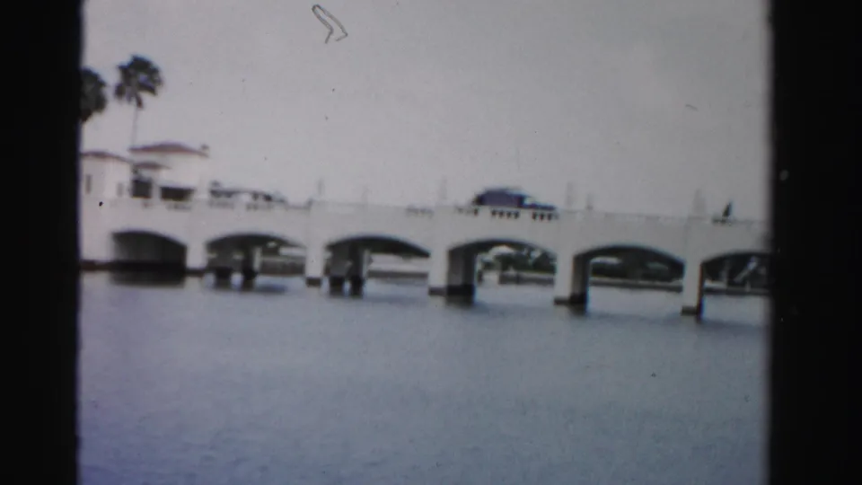 1955 Dade County view of a white multi-arch bridge over still water, with palms and a dark car visible on the span.